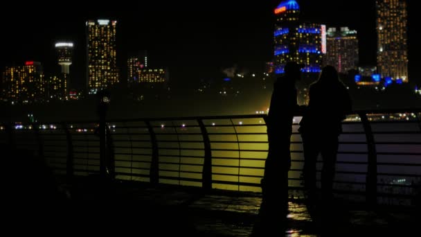Amigos - Homem asiático e mulher caucasiana conversando no fundo da cidade à noite. Pode ser visto silhueta contra os arranha-céus brilhantes — Vídeo de Stock