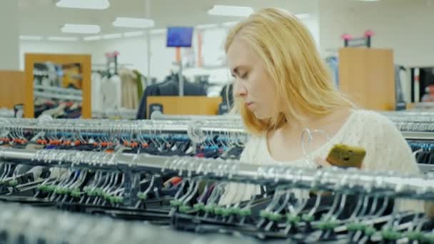 Joven atractiva mujer caucásica elige ropa en la tienda — Vídeos de Stock