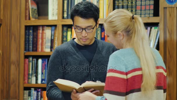 Amigos a falar na biblioteca da faculdade. Homem asiático e mulher caucasiana atraente — Vídeo de Stock