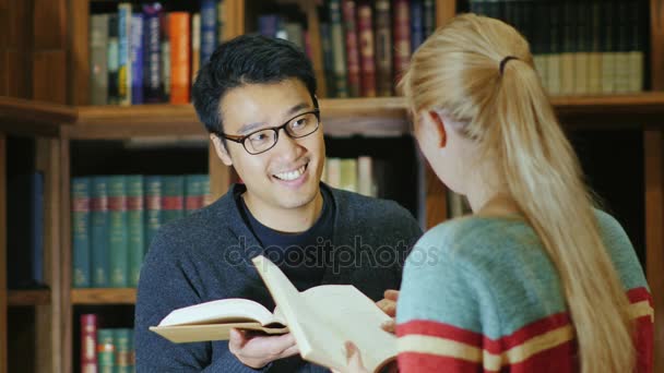 Koreai férfi szemüveg egy nő beszél a könyvtárban. Tanuljunk együtt meg — Stock videók
