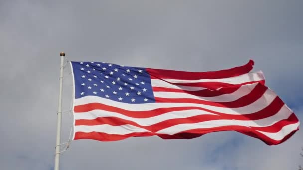 Gran bandera estadounidense sobre un fondo de cielo gris, bellamente iluminado por el sol — Vídeo de stock