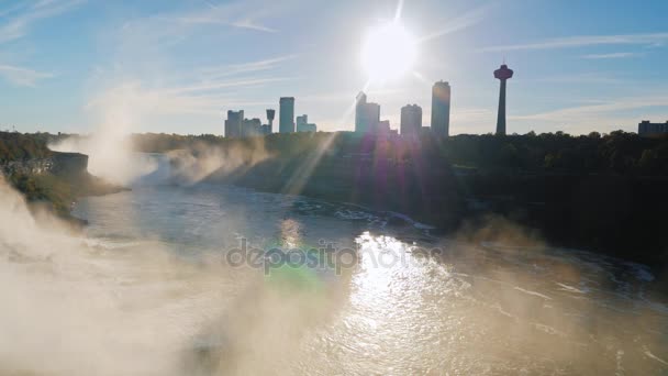 Beautiful sunset over Niagara Falls, view from above. The suns rays shine through the skyscrapers to the Canadian side of the river. Pan shot — Stock Video