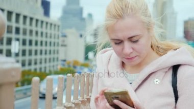 New York'ta bir genç kadının portresi. Pembe ceket Smartphone'da yazarak Manhattan binaların arka plan üzerinde olması gerektiği