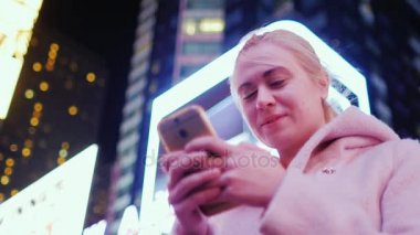Times Square, New York. Gökdelenler geceleri arka plan üzerinde beyaz bir kadın portresi. Gülümseyen smartphone sahiptir