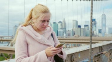 Genç kadın, smartphone cep telefonu ile korkuluk New York'ta Brooklyn Köprüsü'nün ayakta, bir sms tipik