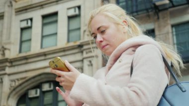 Genç kadın portresi bir akıllı telefon kullanır. Kentsel peyzaj, New York tipik yüksek katlı binalarda arka planı
