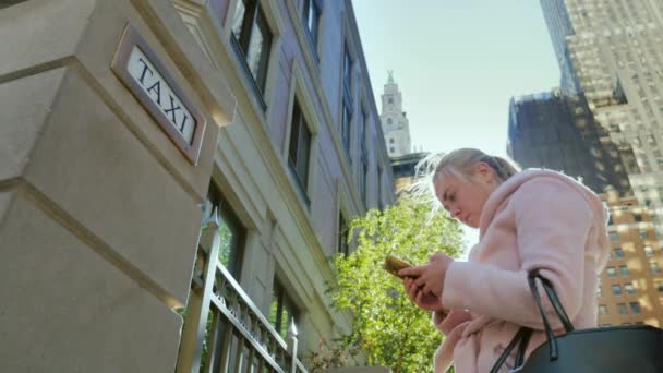 纽约，美国。一名年轻女子使用智能手机上的摩天大楼和一个出租车的标志与标志背景 — 图库视频影像