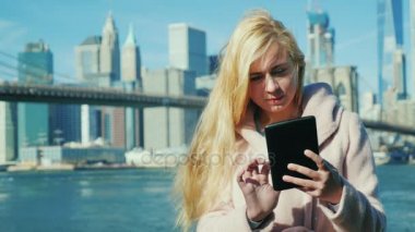 Genç kadın bir tablet PC'de yazarak. Brooklyn Köprüsü nden ve New York City'deki Manhattan siluetinin arka planı
