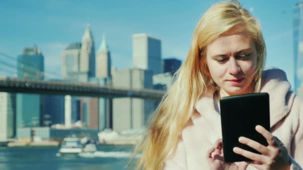 Portret młodej kobiety korzysta z tabletu. Na tle Manhattan i Brooklyn Bridge — Wideo stockowe