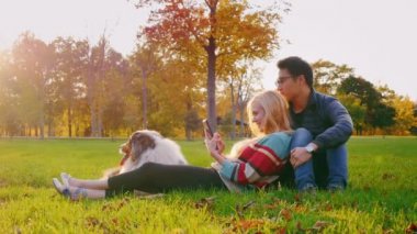 Genç çok etnik gruptan oluşan bir çift rahatlatıcı köpeğiyle parkta. Kafkas kadın tablet sahiptir, yakındaki bir Kore adam oturuyor