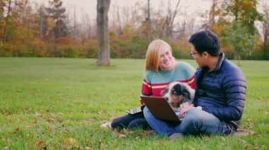 Parkta bir dizüstü bilgisayar ile çalışan genç bir Asyalı adam. Çekici bir kadın ve bir köpek ekrana bakarak yakın