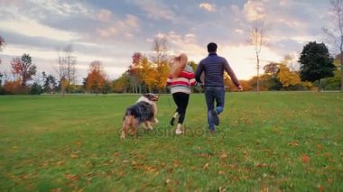 Sevgili senin köpek ile eğlenin. Parkta çalışan genç çok etnik gruptan oluşan bir çift. Steadicam ağır çekim vurdu. Arkadan Görünüm
