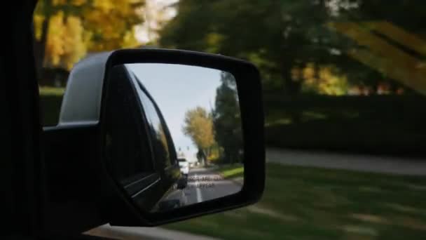 Conduciendo en un típico pueblo americano. En el marco del espejo retrovisor. Día claro de otoño, el sol da hermosos reflejos — Vídeos de Stock