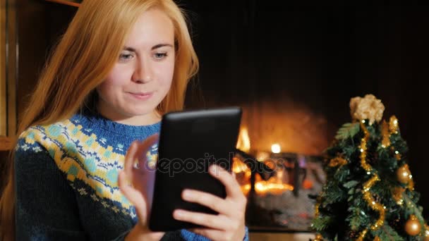 Молодая женщина использует табличку возле елки на фоне огня — стоковое видео