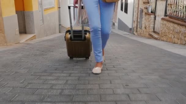 Um turista caminha pela rua estreita da antiga cidade europeia. Na imagem pernas visíveis e saco de viagem sobre rodas, em seguida, a câmera se move para o rosto — Vídeo de Stock