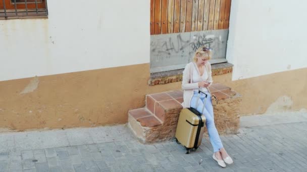 Mujer joven con teléfono se sienta al lado de su bolsa de viaje. Euro-viaje — Vídeos de Stock