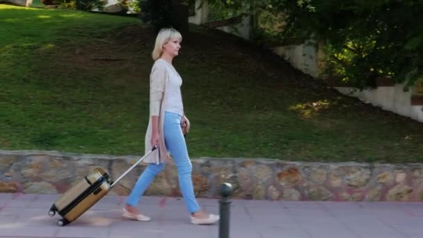 Woman with travel bag goes down the resort area. On a clear sunny day — Stock Video