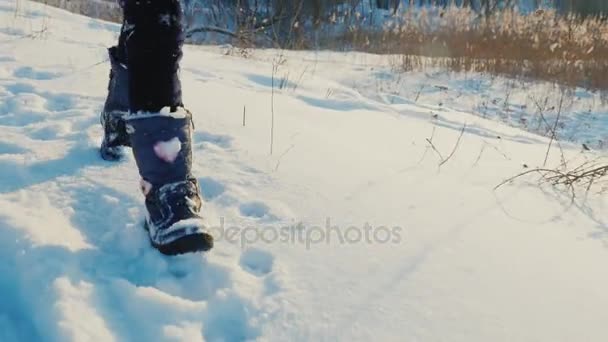 Un niño corre divertido sobre nieve fresca. En la imagen se pueden ver solo las piernas en botas — Vídeo de stock