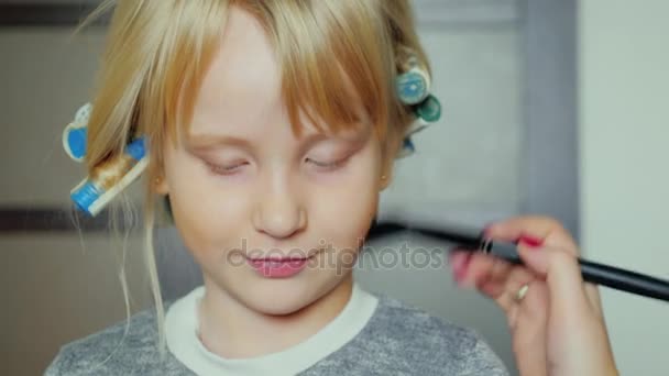 Niña alegre con rulos en la cabeza maquillándose. Nos estamos preparando para unas vacaciones para niños. — Vídeo de stock