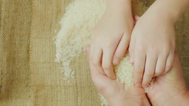 Руки взрослой женщины, держащей зерно риса, над ними, как детские руки, держащие рис — стоковое видео