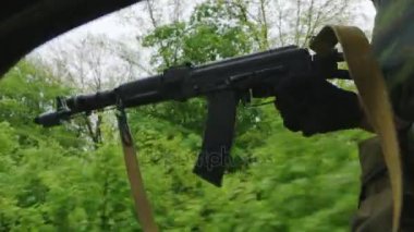 Silahlı adam arabadan dışarı gider. İç görünüm, çerçeve içinde görülen silah ve yeşil çalılar hızlı hareket eden olabilir