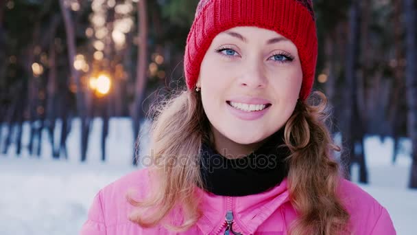 冬の森で若い魅力的な白人女性の肖像画。彼は夕日を背景にカメラに微笑んでいます — ストック動画