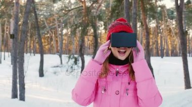 Sanal gerçeklik gözlüklü genç kadın. Etrafa karla kaplı ormanda: kar taneleri yakalamak. Kış eğlence ve teknolojileri