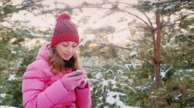 Genç kadın kış ormanda bir cep telefonu kullanarak. Ayrıca bir fincan sıcak çay tutarak. Her zaman bağlı