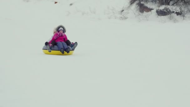 Η γυναίκα με το παιδί κάτω από ένα λόφο σε ένα φουσκωτό κύκλος του σωλήνα. Γέλιο, κουνώντας τα χέρια τους στη φωτογραφική μηχανή. Διασκέδαση χειμώνα — Αρχείο Βίντεο
