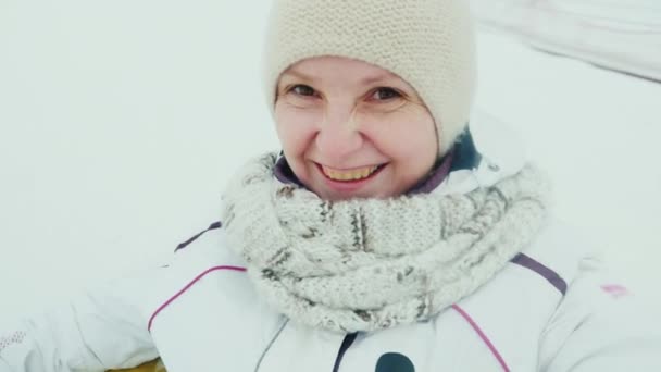 Retrato de una mujer que baja de las colinas cubiertas de nieve. Sentado en un tubo inflable, haciendo selfie, gira alrededor del fondo — Vídeo de stock