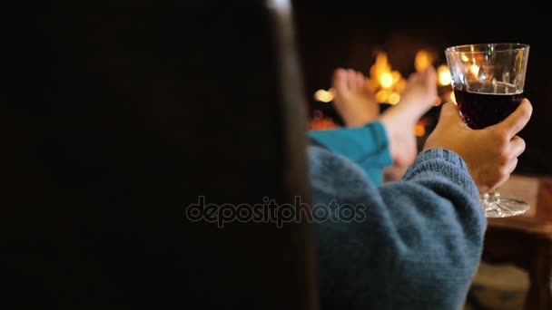 Man with a glass of wine sitting by the fireplace, warm feet. cozy house — Stock Video