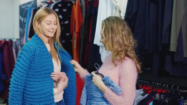 Två unga kvinnor väljer kläder i en butik. Kommunicera, tittar på framtida inköp — Stockvideo