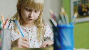 Beş yıl sarışın kız çizer. Ön planda bir vazo ile kalemler
