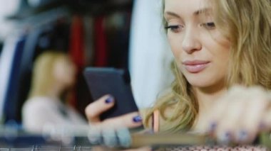 Genç bir kadın portresi bir mağazada elbise seçer, bir smartphone sahiptir