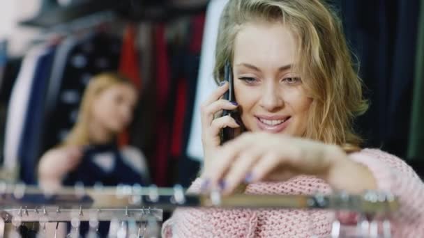 Retrato de una mujer joven elige un vestido en la tienda, hablando en un teléfono celular . — Vídeos de Stock