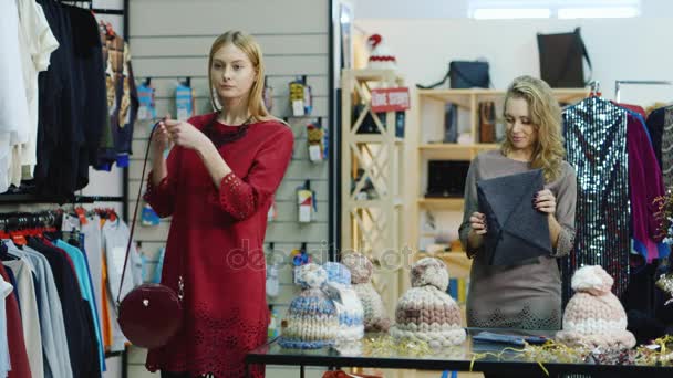 Loja de roupas de mulher elegante. Duas mulheres clientes escolhem produtos - bolsas e acessórios — Vídeo de Stock