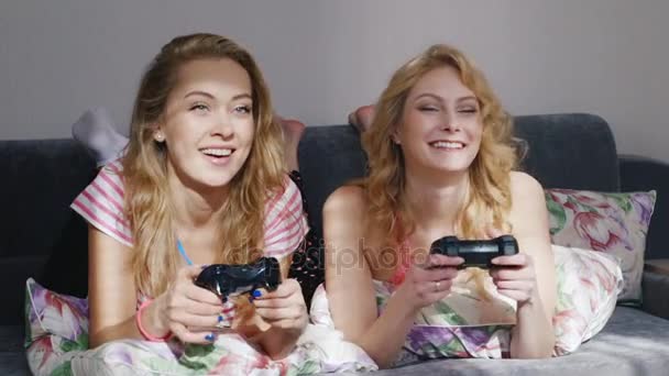 Zwei junge Freundinnen spielen an der Computerkonsole. Zuhause im Schlafanzug auf dem Bett liegen — Stockvideo
