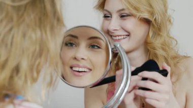 Evde makyaj yapıyor, gülüyor iki genç kadın arkadaşlar. Yüzünü aynaya yansıyan. Pijama partisine bir yatak odasında