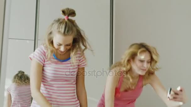 Дві молоді подружки підлітки вчаться танцювати смішні танці. Подивіться на екран мобільного телефону і повторіть рух. піжамна вечірка — стокове відео
