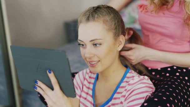 Portret van een jonge vrouw met een tablet. Thuis ontspannen, doet de vriendin haar haren - vlechten vlecht — Stockvideo