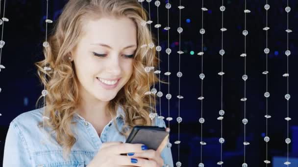 Mujer joven escribiendo un mensaje en un teléfono inteligente. Debe ser en un club nocturno sobre la decoración de perlas de vidrio — Vídeos de Stock