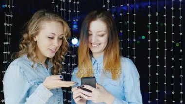 İki genç kadın arkadaşlar smartphone bir gece kulübünde kullanın.