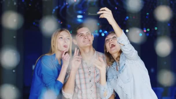 Des amis de jeunes riant, prenant des photos d'eux-mêmes dans une boîte de nuit - un garçon et deux jolies femmes — Video