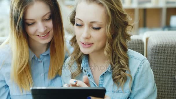 Portret van twee jonge aantrekkelijke vrouwen gebruiken een tablet of een laptop in een café. — Stockvideo