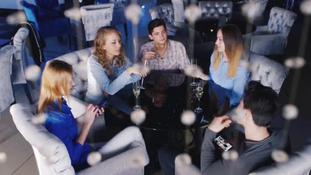 Jóvenes relajándose en una cafetería, disfrutando de un smartphone, bebiendo champán de copas de vino — Vídeo de stock