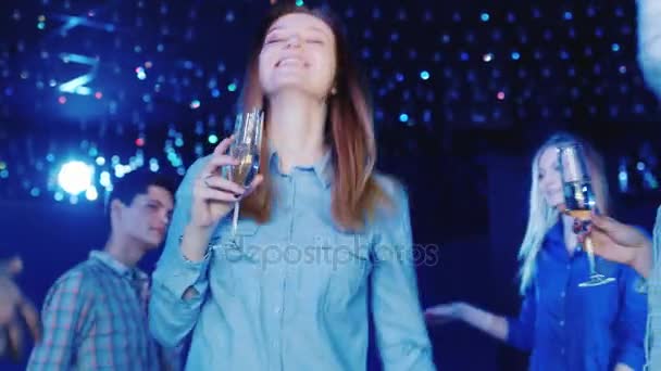 Ελκυστική γυναίκα με μακριά μαλλιά που χορεύουν σε ένα νυχτερινό κέντρο διασκέδασης. Κρατάει στο χέρι του ένα ποτήρι από το ποτό — Αρχείο Βίντεο