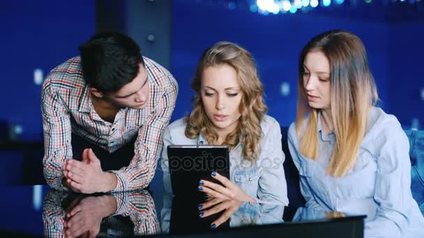 三个朋友，一名年轻男子和平板电脑屏幕上寻找有兴趣的两个女人。俯身在一家咖啡馆表 — 图库视频影像