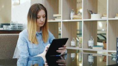 Genç kadın bir kafede bir masada oturan bir tablet üzerinde okuma