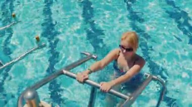 Havuzun vücudunuzdaki tren. Genç bir kadın bir mayo bir eğitim oturumu üzerinde simülatörü havuzda eşlik ediyor. Etkin ve sağlıklı yaşam tarzı