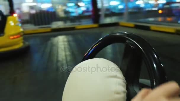 Pov video: Ride a car on an attraction in an amusement park. In the frame, you can see the steering wheel and childrens hands on it, the background is moving fast — Stockvideo